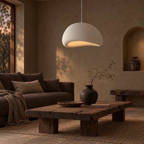 Witte hanglamp met sculpturale lampenkap boven een rustieke houten salontafel.