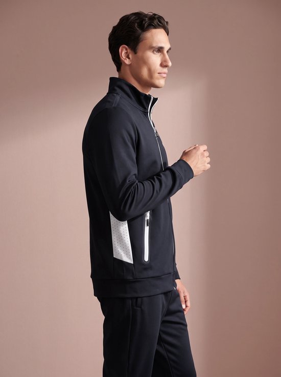 Man in profiel, draagt een zwart sportvest met witte rits en details.