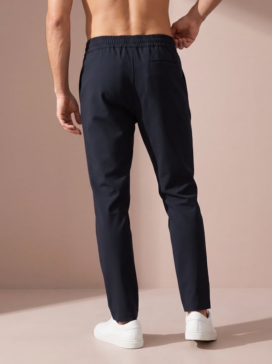 Man van achteren gezien, draagt donkerblauwe sportbroek met witte sneakers.