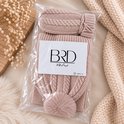 Beige gebreide kinderset met kabelpatroon in verpakking. Muts met pompon en wanten.