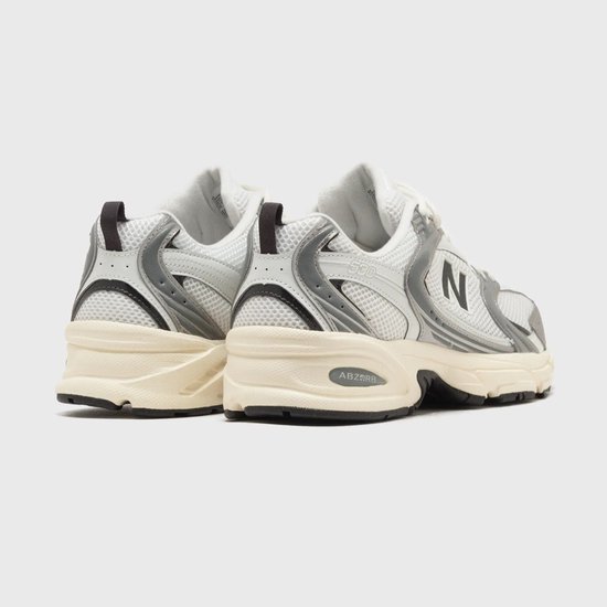 Achterkant van witte New Balance 530 sneakers met zilveren en grijze details.