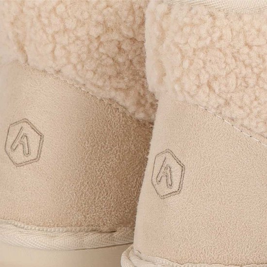 Close-up van de hiel van beige pantoffels met een in reliëf gedrukt zeshoekig merklogo.