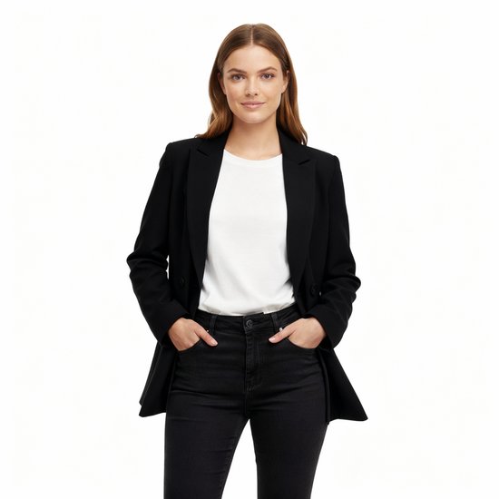 Model draagt een zwarte oversized blazer met open revers, een witte top en een zwarte broek. Handen in de zakken.