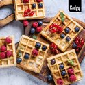 Vier gouden Brusselse wafels, versierd met bosbessen, frambozen en rode bessen op een houten plank.