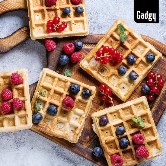 Vier gouden Brusselse wafels, versierd met bosbessen, frambozen en rode bessen op een houten plank.