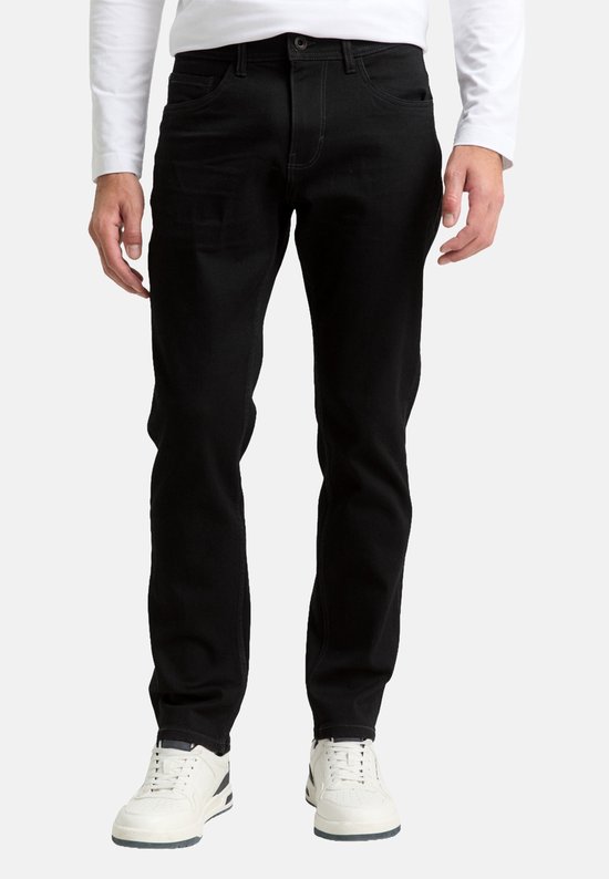 Man in zwarte jeans en witte longsleeve, staand.