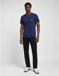 Volledig zicht van een man in een marineblauw T-shirt en zwarte jeans, met witte sneakers met strepen.