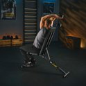 Man in grijs shirt doet een triceps oefening op een zwarte fitnessbank met een dumbbell.