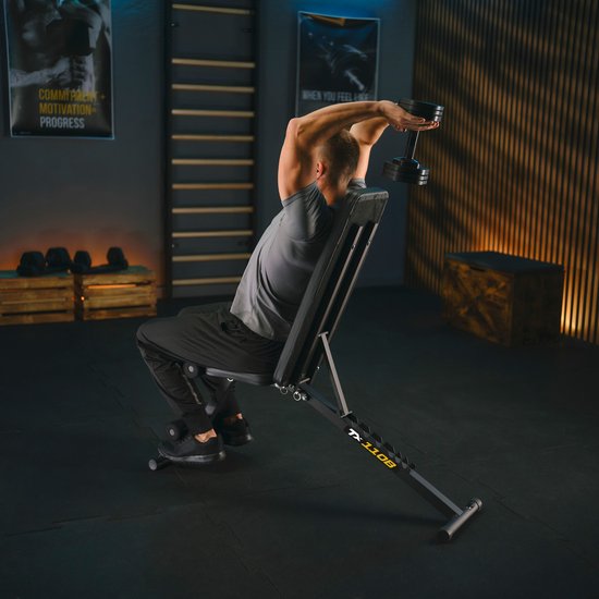Man in grijs shirt doet een triceps oefening op een zwarte fitnessbank met een dumbbell.