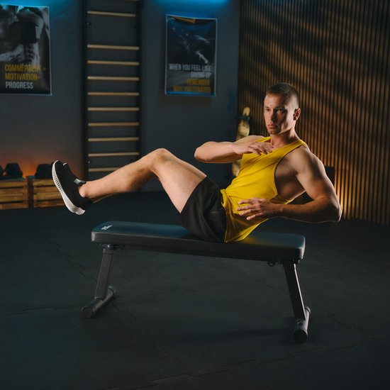 Man met gele tanktop doet een twist crunch op een zwarte trainingsbank.
