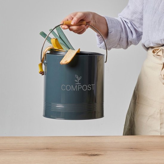 Donkere grijze compostbak met houten handvat, gevuld met bananenschillen, brood en groenten.