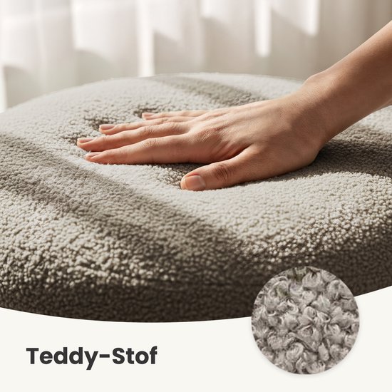 Hand die zacht teddy stof indrukt op een ronde, beige poef. Close-up van de textuur.