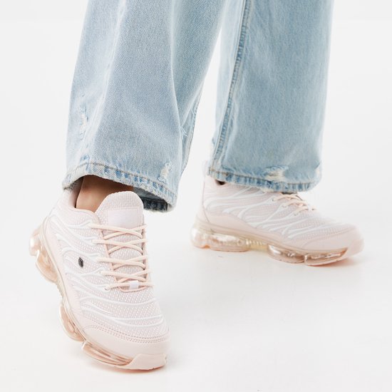 Roze lage sneakers met witte golvende lijnen en doorzichtige zool. Gedragen met een jeans.
