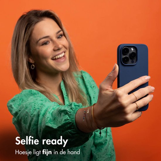 Vrolijke vrouw met blond haar neemt selfie met donkerblauwe telefoonhoes.