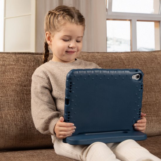 Een jong meisje zit op een bruine bank en houdt een blauwe tablet in een hoes vast.