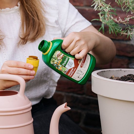Een groene fles Pokon Mediterrane plantenvoeding wordt door een vrouw met gele dop vastgehouden.