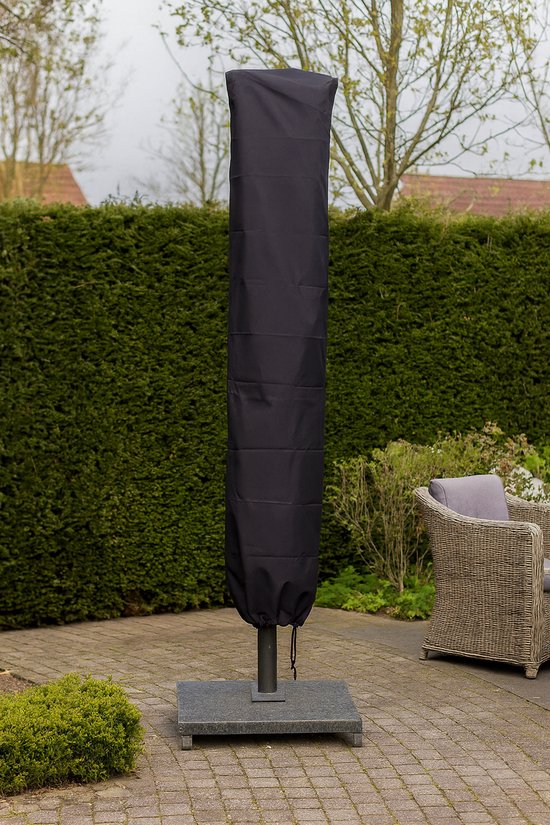 Zwarte parasolhoes, gesloten en rechtopstaand op een voet, in een tuin met struiken en meubilair.