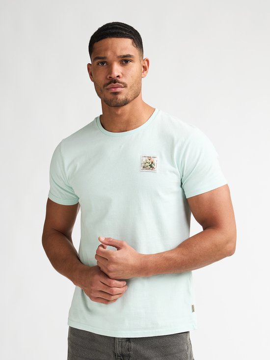 Man in lichtgroen T-shirt met een opgedrukte postzegel met bloemen op de linkerborst.