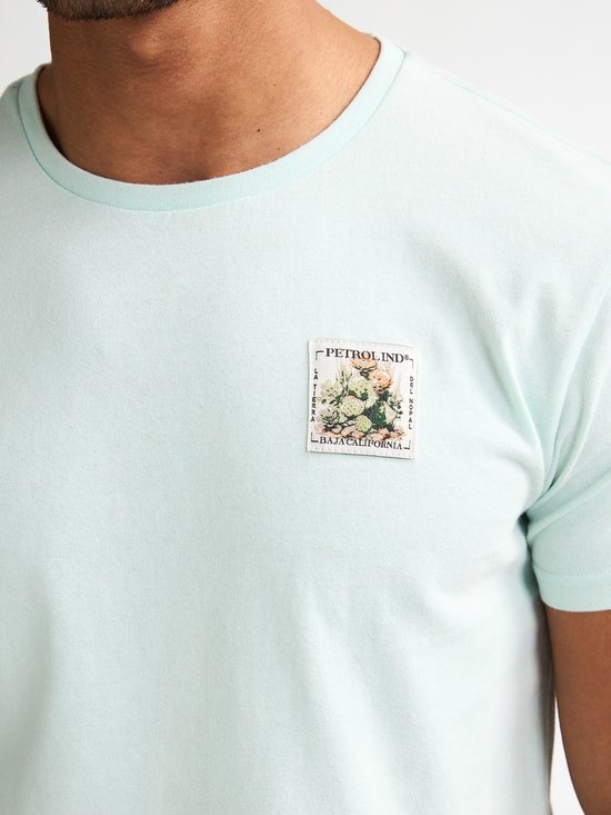 Close-up van een lichtgroen T-shirt met een opgedrukte postzegel met bloemen.