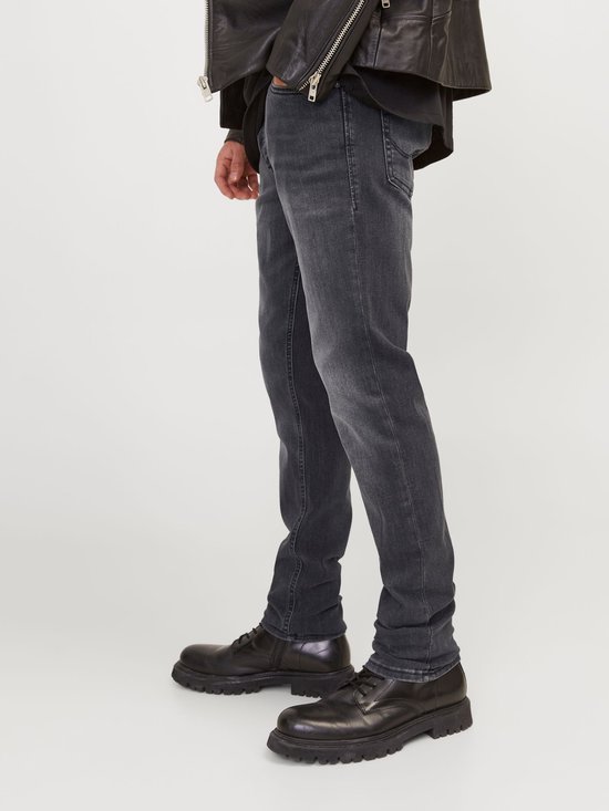 Man met grijze jeans en zwarte laarzen, de broek is opgerold aan de enkel.