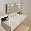 Witte make-upspiegel met verlichting, op een witte console met make-up en een tas.