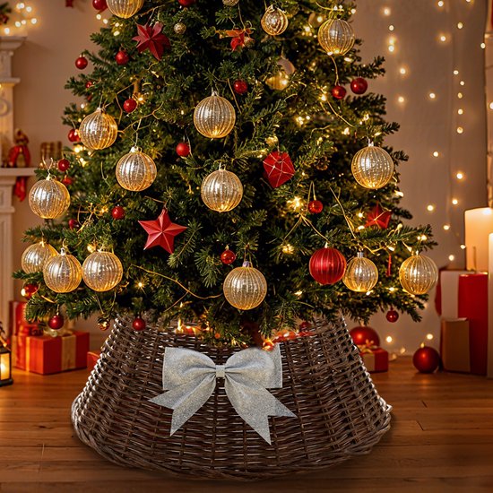 Bruine rieten kerstboommand met zilveren strik onder een verlichte kerstboom vol rode en gouden ballen.