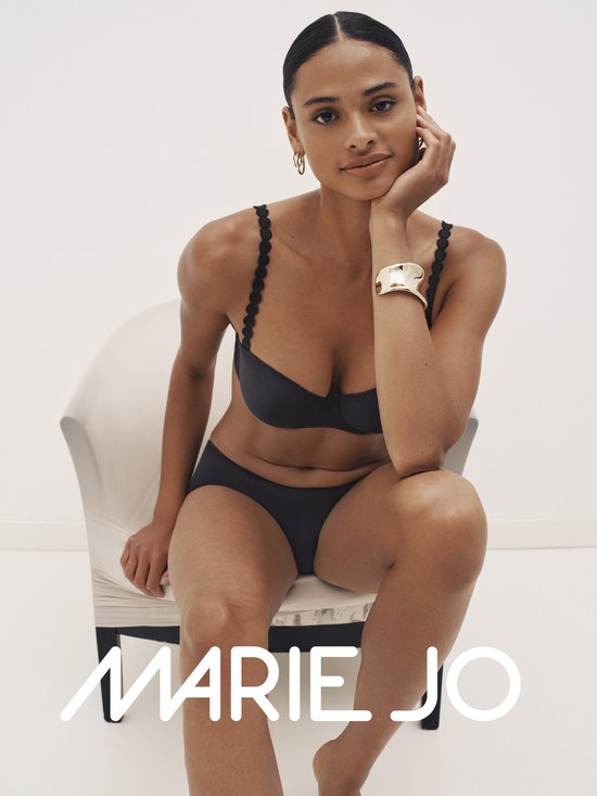 Model zittend op stoel, draagt zwarte strapless bh en bijpassend broekje. MARIE JO logo.