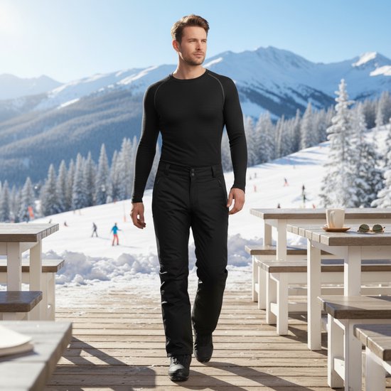 Man in zwart thermoshirt met lange mouwen en skibroek, wandelend op een houten terras in de sneeuw.