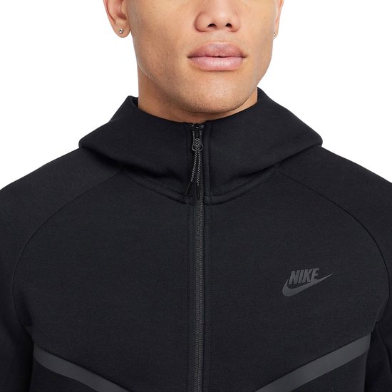 Close-up van de rits en het Nike logo op een zwarte Tech Fleece hoodie.