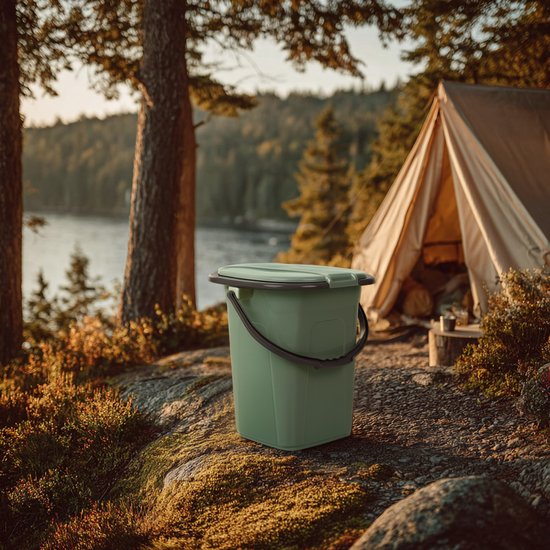 Groene campingtoilet emmer met deksel, staand op rotsen bij een meer en tent.