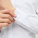 Man sluit de knopen van de manchetten van een wit overhemd.