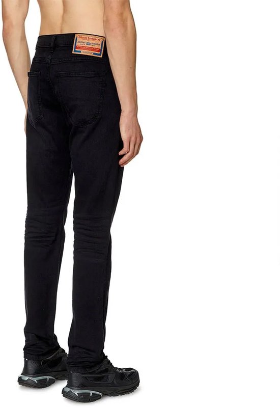 Man in zwarte jeans, van achteren gezien. De broek heeft een label op de achterkant.