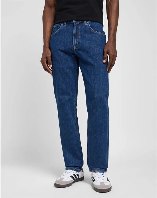Blauwe Lee jeans met rechte pijpen, gedragen door een donkere man met witte sneakers.