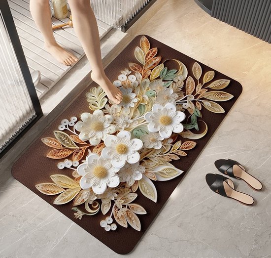 Bruine badmat met een 3D-bloemenmotief van witte en crèmekleurige bloemen en bladeren. Voeten op de mat, slippers ernaast.