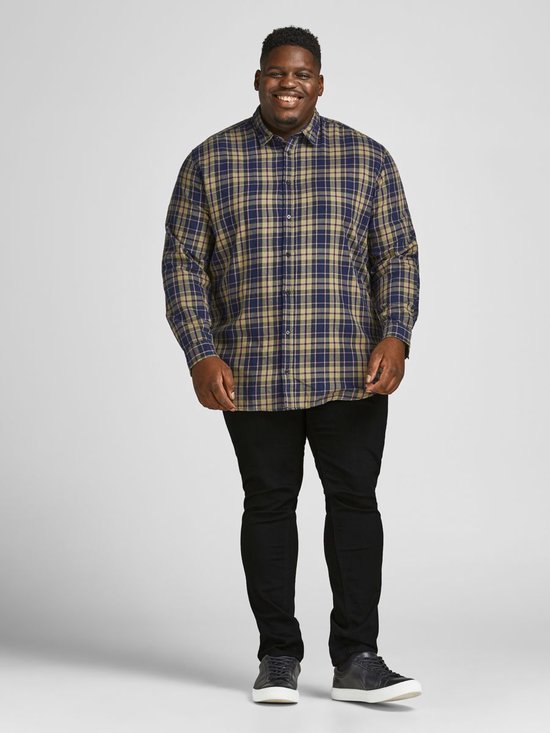 Man met een geruite blouse in blauw, beige en donkerblauw, en zwarte jeans.