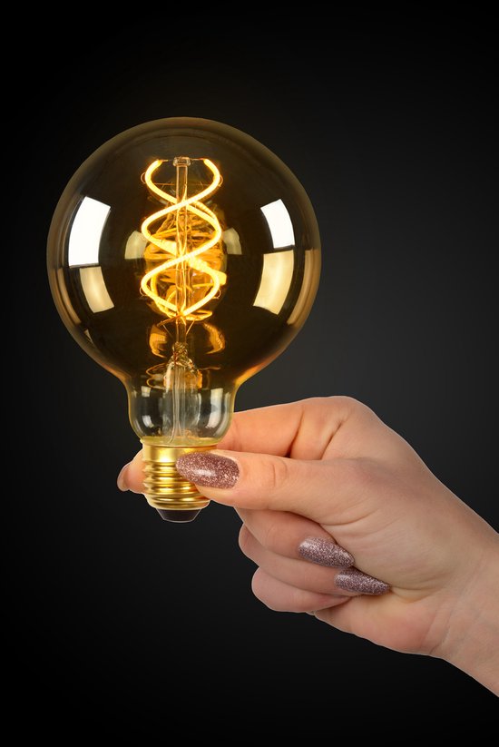Ampoule à filament G95 dorée avec spirale visible, tenue par une main avec vernis à ongles scintillant.