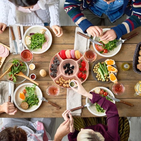 Gevuld roze snackbord met macrons, bessen, tomaten en pinda's op een tafel met eten.