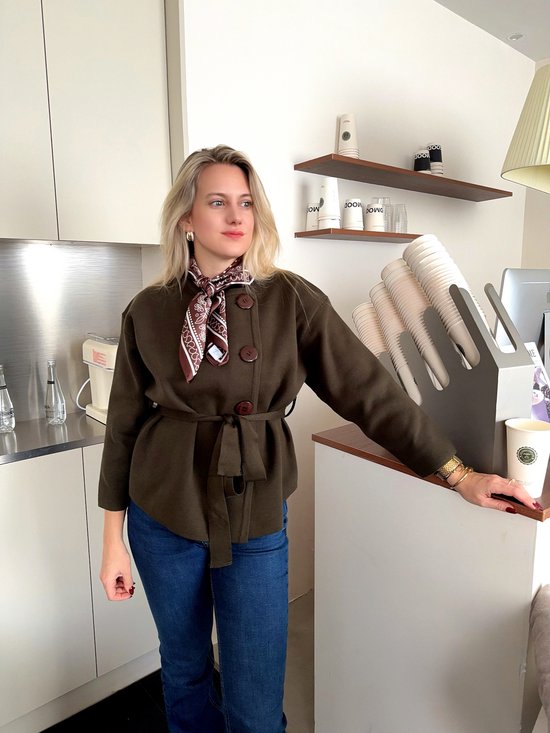 Model draagt een donkerbruine jas met ceintuur en bruin-wit paisley sjaaltje.