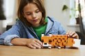 Un garçon à une table en bois regarde le renard LEGO Minecraft constructible qu'il tient.