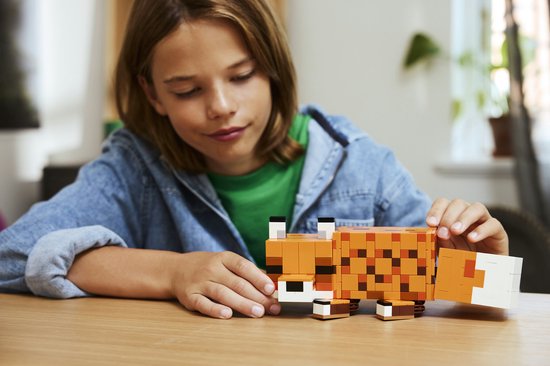 Un garçon à une table en bois regarde le renard LEGO Minecraft constructible qu'il tient.
