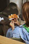 Un garçon en veste en jean et pantalon marron, assis les jambes croisées, tient un renard LEGO Minecraft.