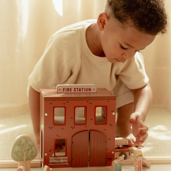 Kind speelt met de rode houten brandweerkazerne met 'FIRE STATION' bord en brandweerwagen.