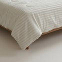 Wit geribd dekbed op een houten bed, de hoek hangt over de zijkant.