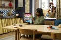 Een vrouw kijkt naar het opgehangen LEGO Art Landschap met Japanse Kersenbloesems, zittend aan een tafel.
