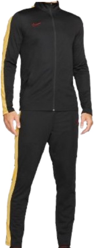 Zwart trainingspak van Nike met gele strepen op de zijkanten van de broek en jas. Een rood Nike logo op de borst.