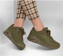 Model draagt legergroene Skechers Uno damessneakers met geruite broek. Zichtbaar luchtkussen in de zool.