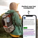 Vrouw met rugzak in de natuur, met een witte Denver radio bevestigd aan de rugzak. Op de telefoon wordt de tekst "Wat zit er in een noodpakket?" getoond.