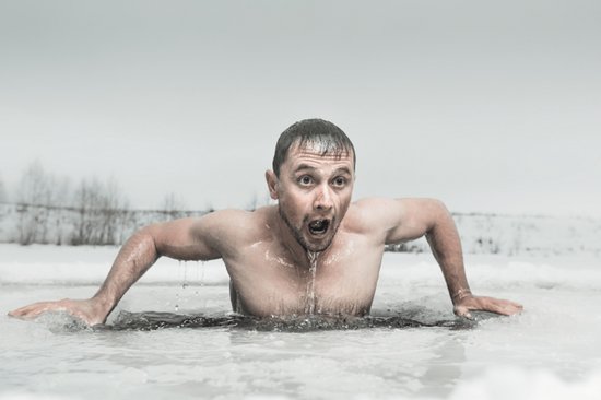 Man stapt uit koud, ijzig water, gezichtsuitdrukking van verbazing en kou.