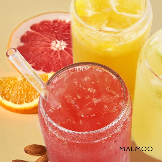 Close-up van een rood drankje met stukjes fruit in een glas met rietje, naast sinaasappel en grapefruit.