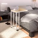 Bijzettafel met lichtbruin houten blad en wit metalen frame, naast een bed.